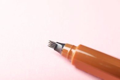 Photo of One liquid eyebrow pencil on light pink background, closeup. Space for text