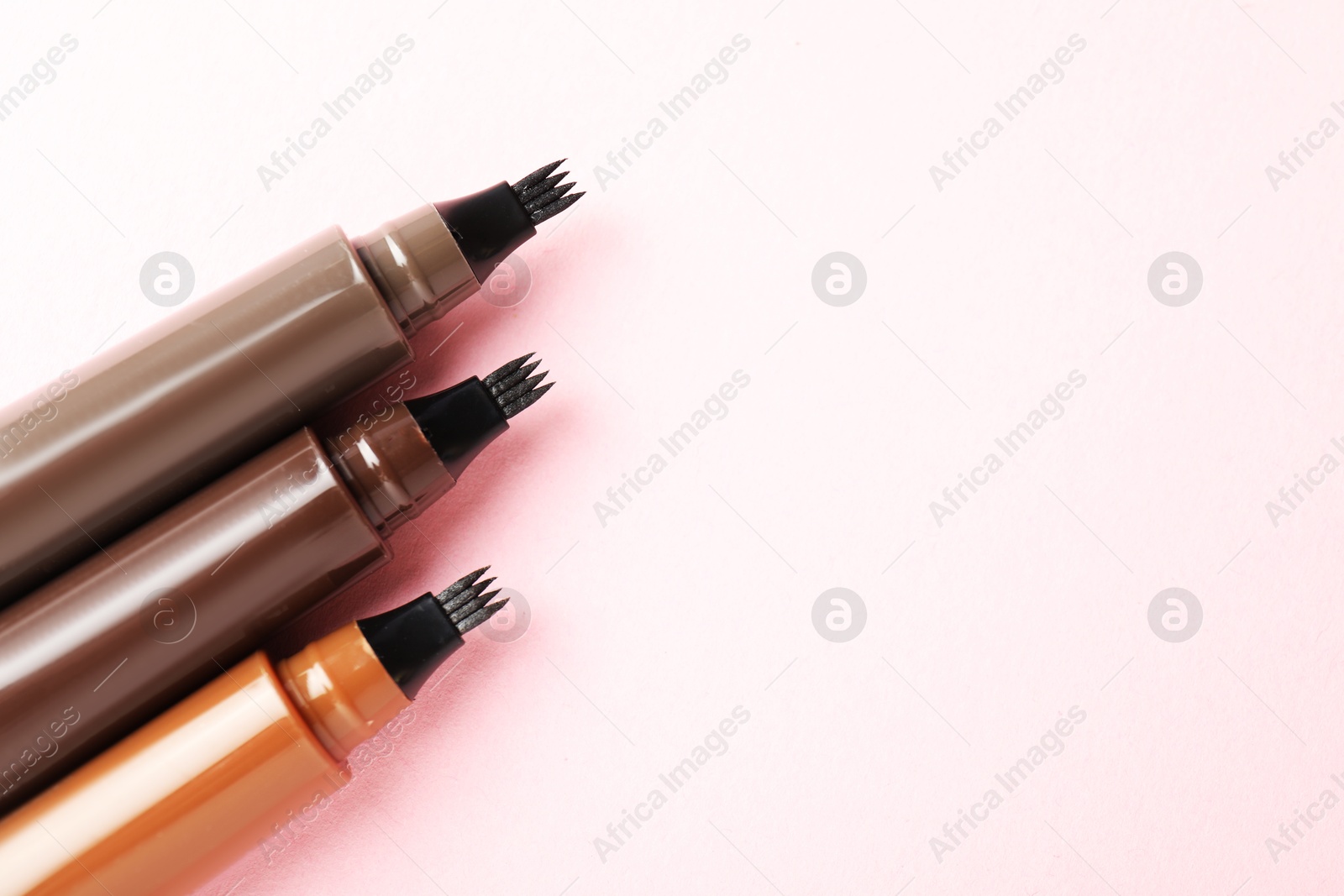 Liquid eyebrow pencils on light pink background, flat lay. Space for text Photo of Liquid eyebrow pencils on light pink background, flat lay. Space for text