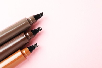 Photo of Liquid eyebrow pencils on light pink background, flat lay. Space for text