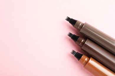 Photo of Liquid eyebrow pencils on light pink background, flat lay. Space for text