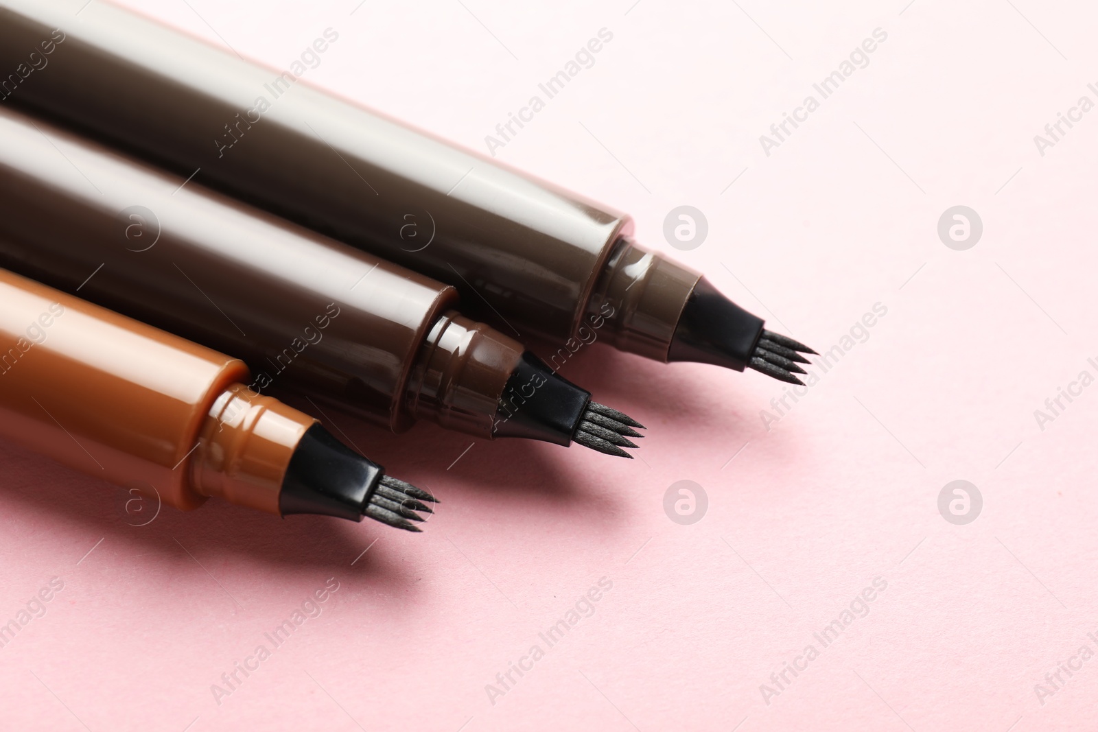 Liquid eyebrow pencils on light pink background, closeup Photo of Liquid eyebrow pencils on light pink background, closeup