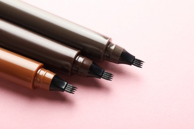 Photo of Liquid eyebrow pencils on light pink background, closeup