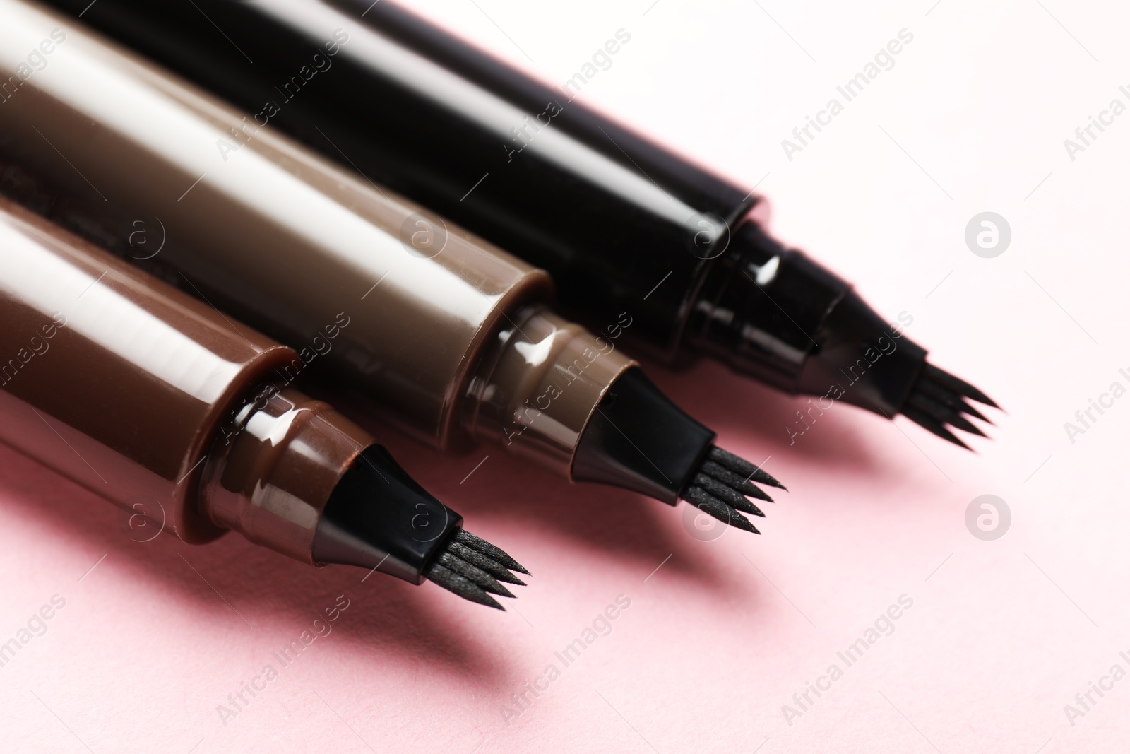 Liquid eyebrow pencils on light pink background, closeup Photo of Liquid eyebrow pencils on light pink background, closeup