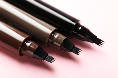 Photo of Liquid eyebrow pencils on light pink background, closeup