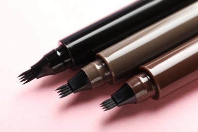 Photo of Liquid eyebrow pencils on light pink background, closeup