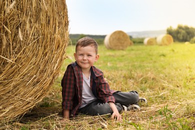 Photo of Little boy near hay bale in field at summer. Space for text