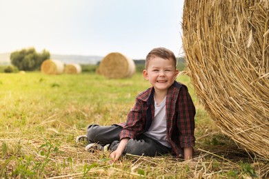 Photo of Little boy near hay bale in field at summer. Space for text