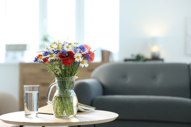 Photo of Beautiful wildflowers in vase, water and book on wooden table at home. Space for text
