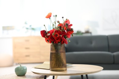 Photo of Beautiful poppy flowers in vase and book on wooden table at home