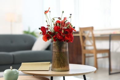 Photo of Beautiful poppy flowers in vase and book on wooden table at home