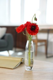 Photo of Beautiful poppy flowers in vase and book on wooden table at home