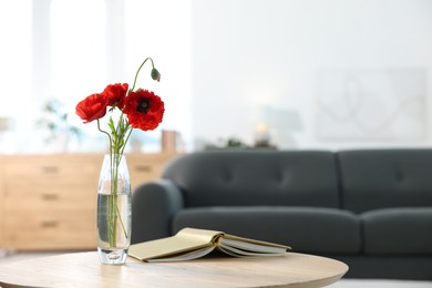 Photo of Beautiful poppy flowers in vase and book on wooden table at home. Space for text