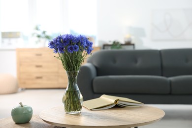 Photo of Beautiful blue cornflowers in vase and book on wooden table at home. Space for text