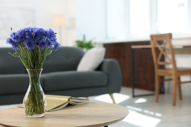 Photo of Beautiful blue cornflowers in vase and book on wooden table at home. Space for text