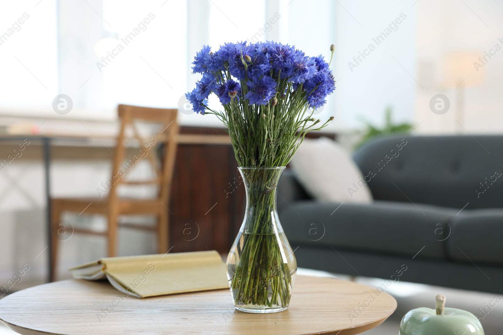 Beautiful blue cornflowers in vase and book on wooden table at home Photo of Beautiful blue cornflowers in vase and book on wooden table at home