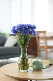 Photo of Beautiful blue cornflowers in vase and book on wooden table at home