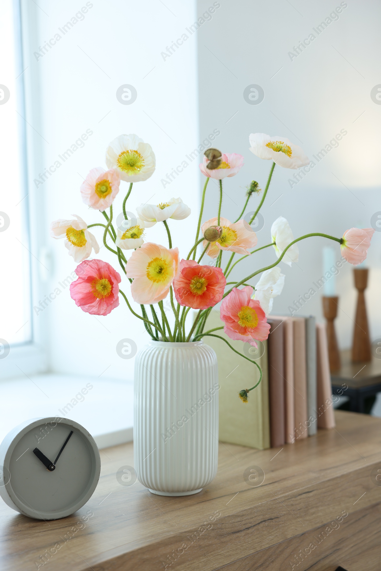 Beautiful poppy flowers, clock and books on wooden table indoors Photo of Beautiful poppy flowers, clock and books on wooden table indoors