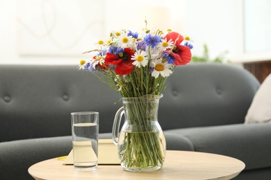 Photo of Beautiful wildflowers in vase and water on wooden table at home