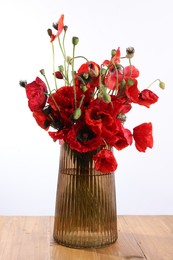 Photo of Beautiful red poppy flowers in vase on wooden table against white background