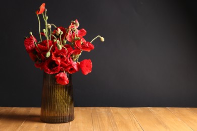 Photo of Beautiful red poppy flowers in vase on wooden table against black background. Space for text