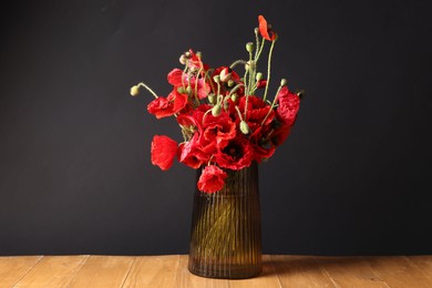 Photo of Beautiful red poppy flowers in vase on wooden table against black background