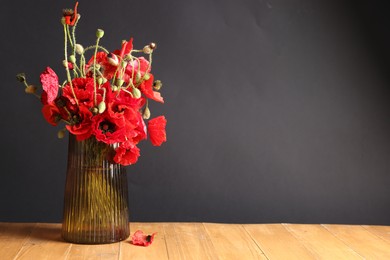 Photo of Beautiful red poppy flowers in vase on wooden table against black background. Space for text