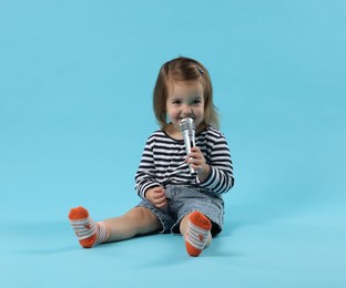 Photo of Cute little girl with microphone on light blue background