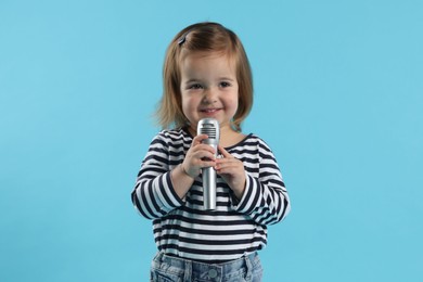 Photo of Cute little girl with microphone on light blue background