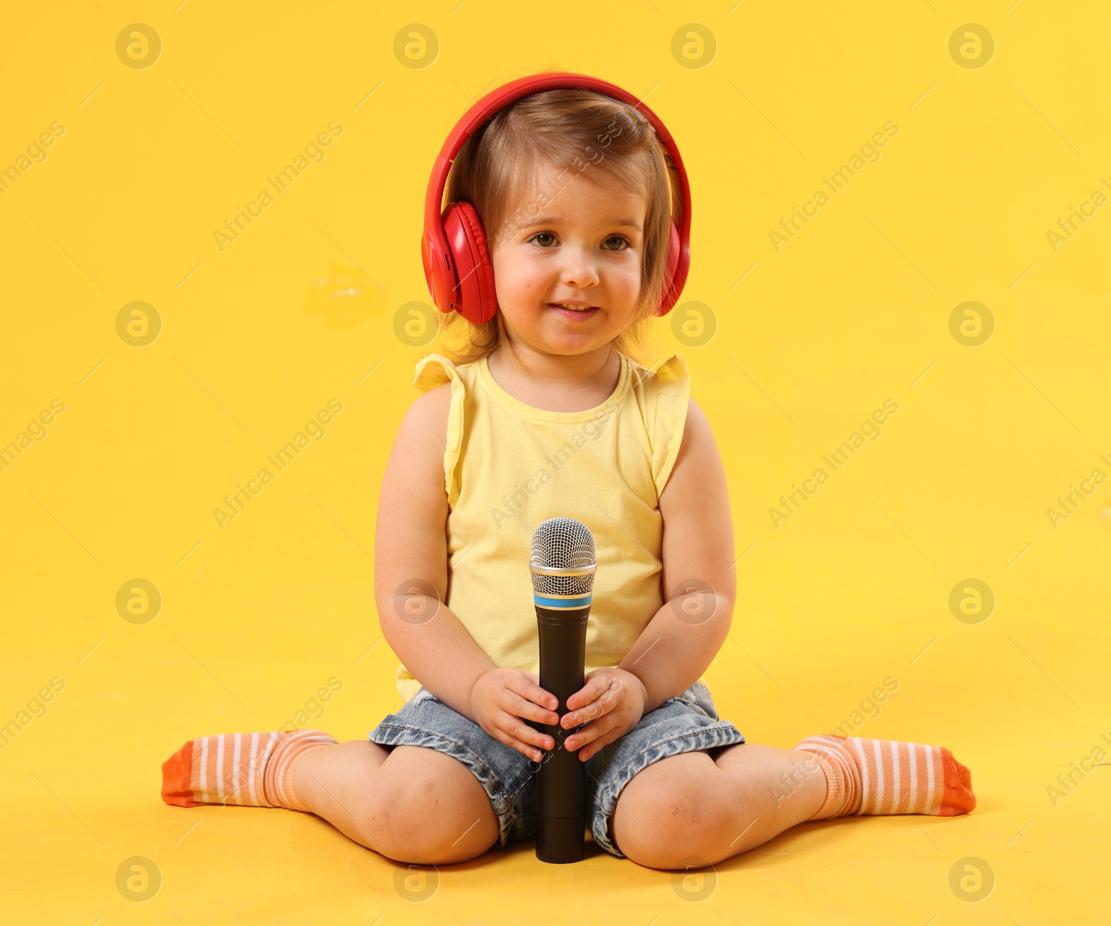 Cute little girl with headphones and microphone on yellow background Photo of Cute little girl with headphones and microphone on yellow background