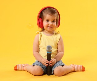 Photo of Cute little girl with headphones and microphone on yellow background