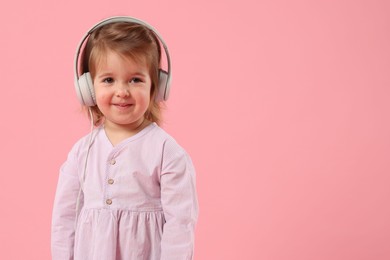 Photo of Cute little girl in headphones on pink background, space for text