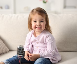 Photo of Cute little girl with microphone on sofa at home