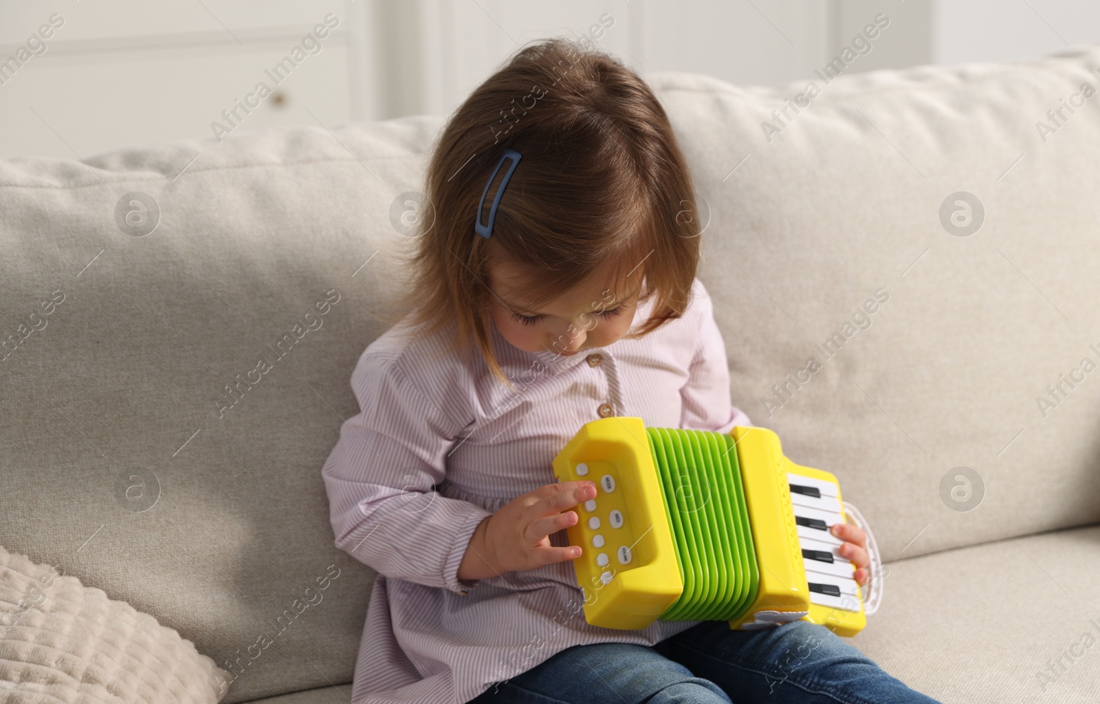 Cute little girl playing toy accordion on sofa at home Photo of Cute little girl playing toy accordion on sofa at home