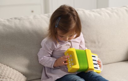 Photo of Cute little girl playing toy accordion on sofa at home