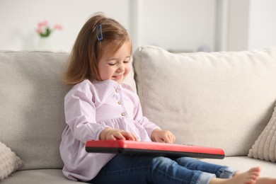 Photo of Cute little girl playing toy electric piano on sofa at home