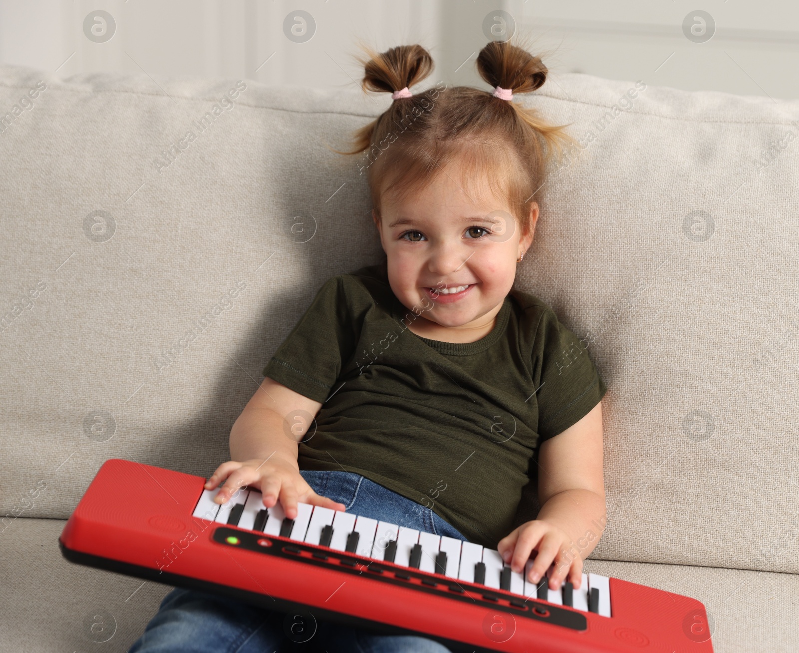 Cute little girl playing toy electric piano on sofa at home Photo of Cute little girl playing toy electric piano on sofa at home