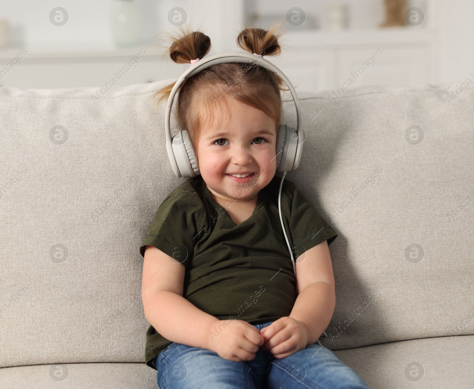 Cute little girl in headphones on sofa at home Photo of Cute little girl in headphones on sofa at home