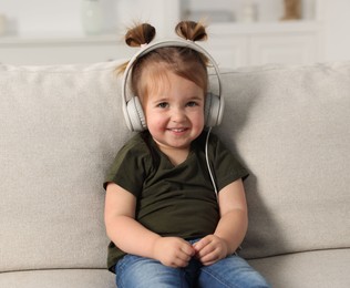 Photo of Cute little girl in headphones on sofa at home