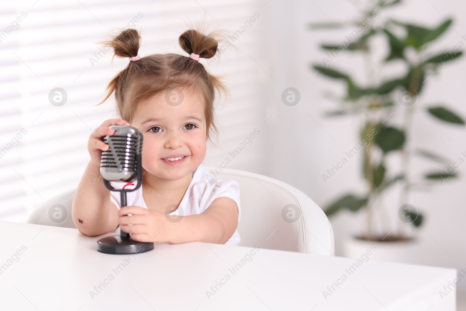 Cute little girl with microphone on at table indoors Photo of Cute little girl with microphone on at table indoors