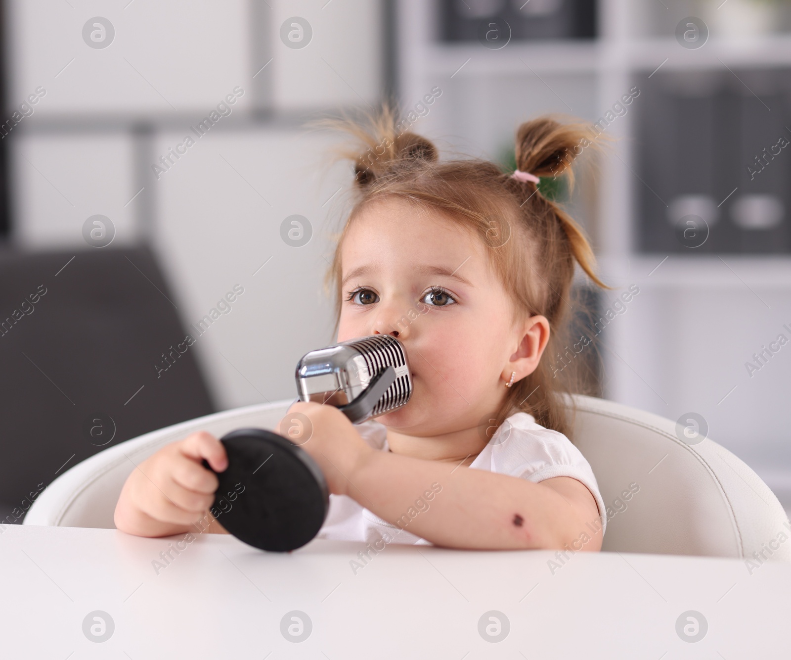 Cute little girl with microphone on at white table indoors Photo of Cute little girl with microphone on at white table indoors