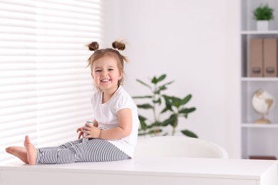 Photo of Cute little girl with microphone on table at home, space for text