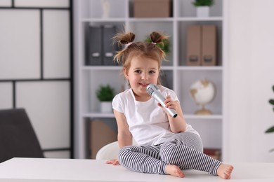 Photo of Cute little girl with microphone on white table at home, space for text