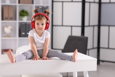 Photo of Cute little girl in headphones on white table at home, space for text