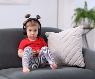 Photo of Cute little girl in headphones on sofa at home
