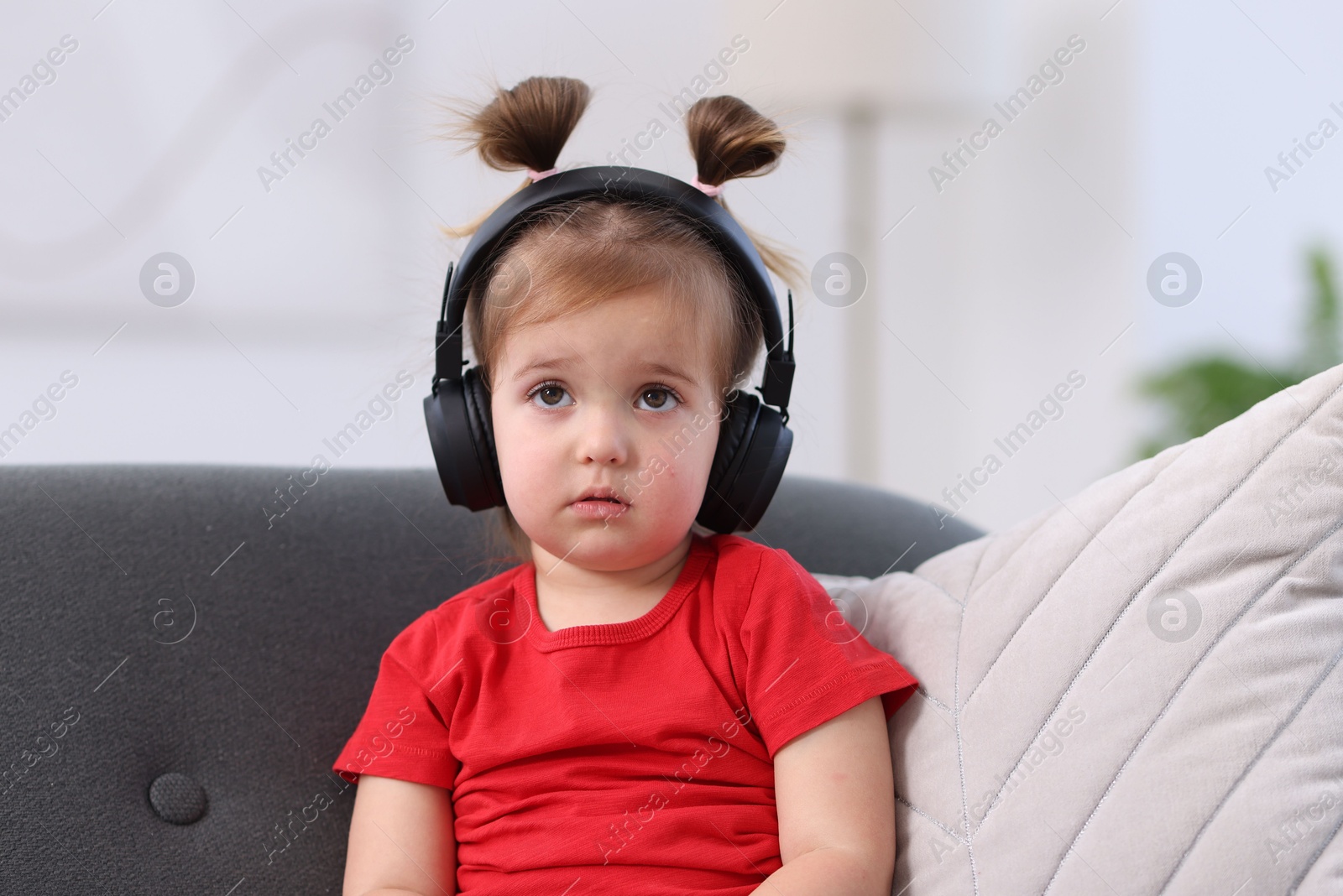 Photo of Cute little girl in headphones on sofa at home