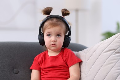Photo of Cute little girl in headphones on sofa at home