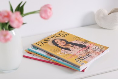 Photo of Many different trendy magazines and tulip flowers on white cabinet indoors, closeup