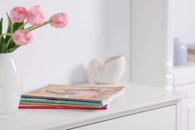Photo of Many different trendy magazines and tulip flowers on white cabinet indoors, closeup
