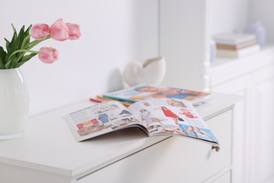 Photo of Many different trendy magazines and tulip flowers on white cabinet indoors