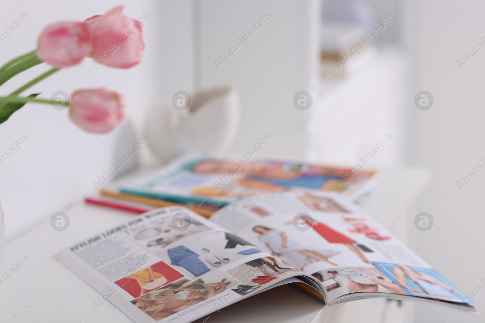 Many different trendy magazines and tulip flowers on white cabinet indoors, closeup Photo of Many different trendy magazines and tulip flowers on white cabinet indoors, closeup
